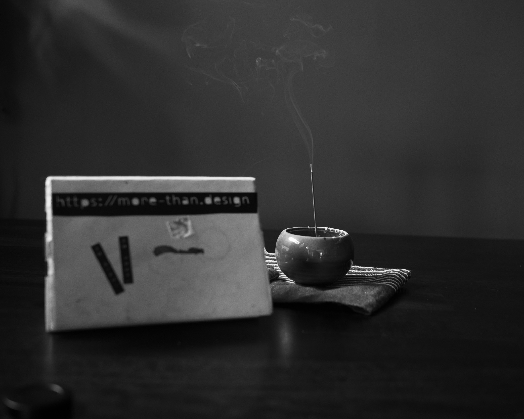 Christian Solorzano — black-and-white still life of a zine reading more-than.design beside a ceramic incense bowl with rising smoke