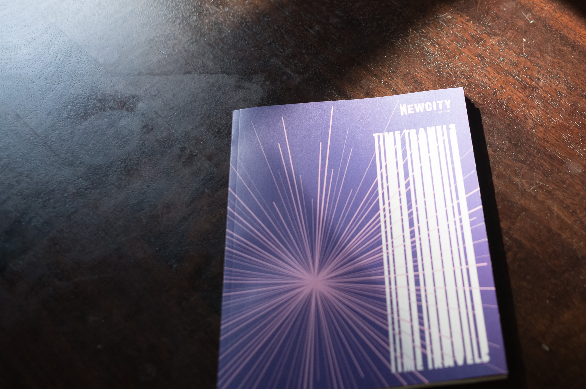 Christian Solorzano — photograph of a NEWCITY "Time Travels" issue with a starburst cover on a dark wooden table