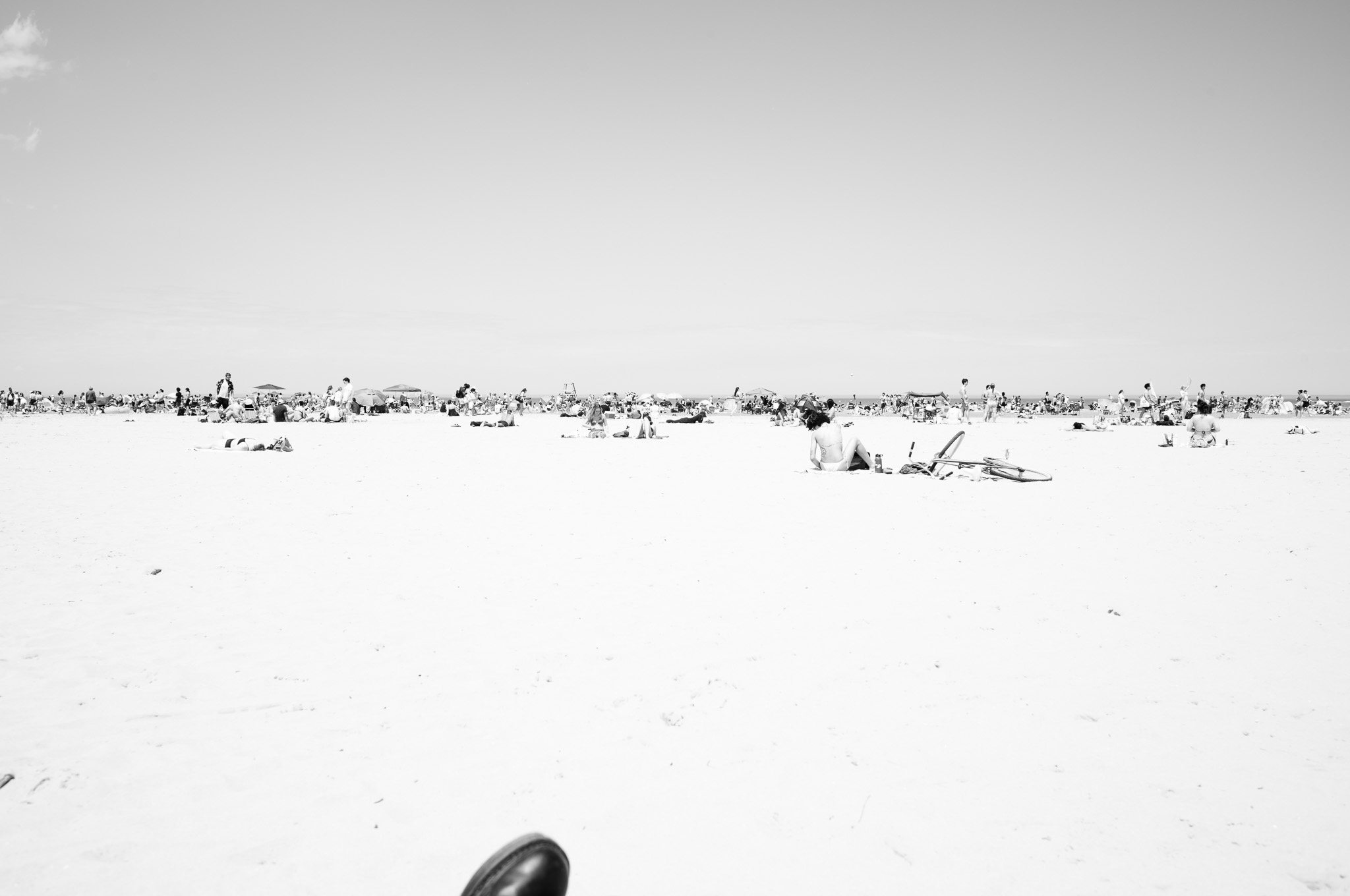 Christian Solorzano — black-and-white photograph of a sunlit, crowded beach stretching to the horizon, viewed from low on the sand