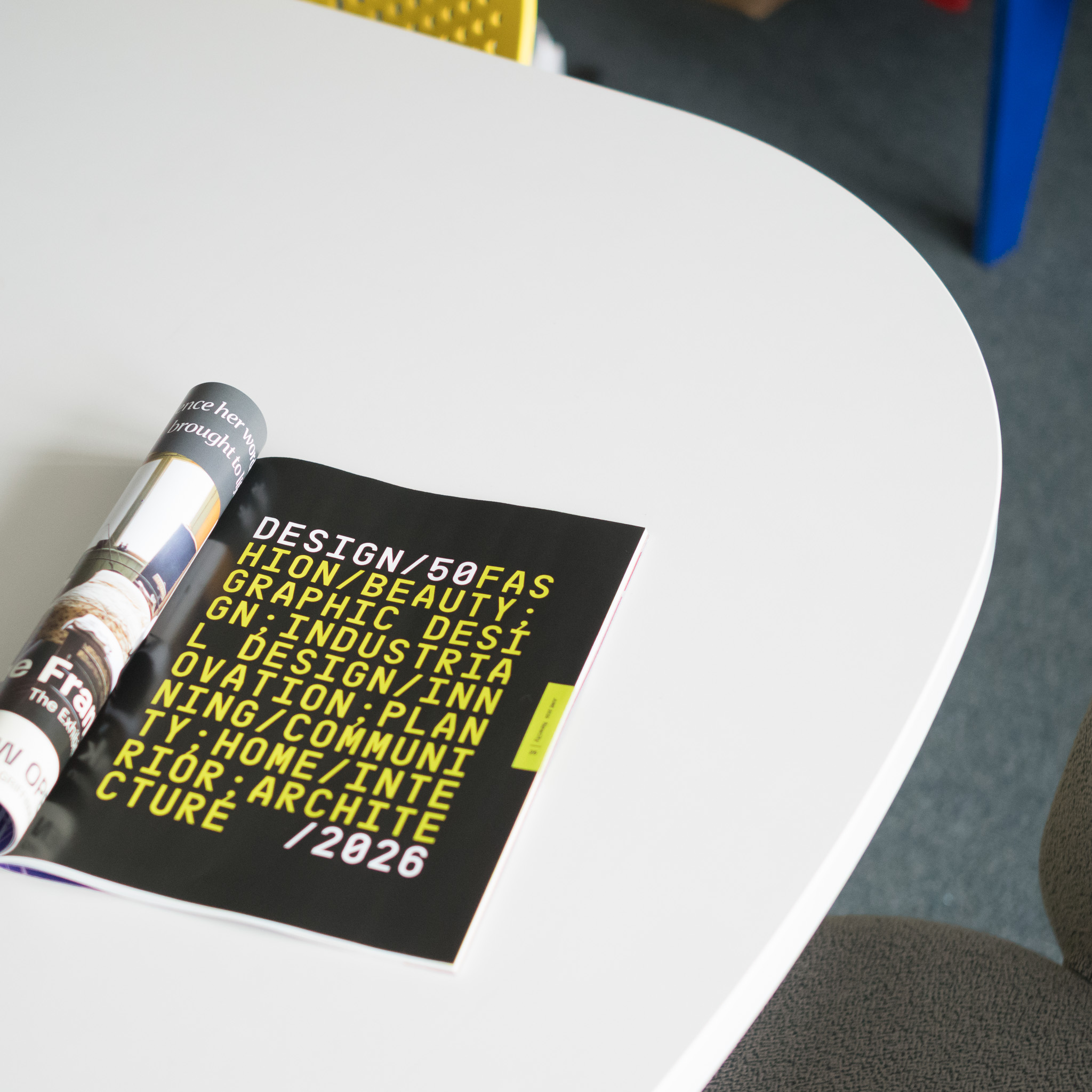 Christian Solorzano — photograph of the NEWCITY Design 50 booklet open to a bold yellow type page listing the design disciplines, on a white round table
