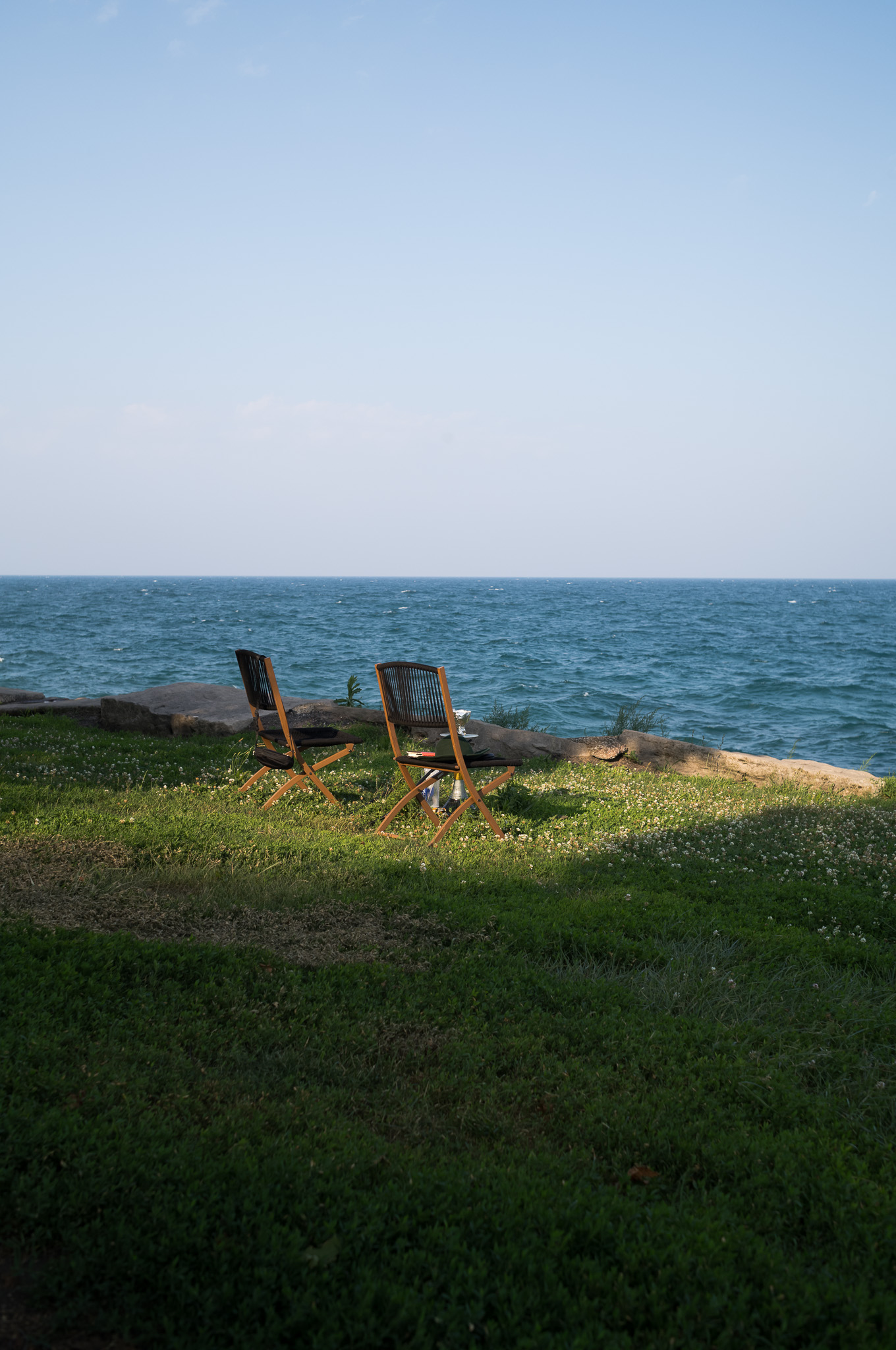 Christian Solorzano — photograph of two empty folding chairs on the grass facing the open blue water of the lake