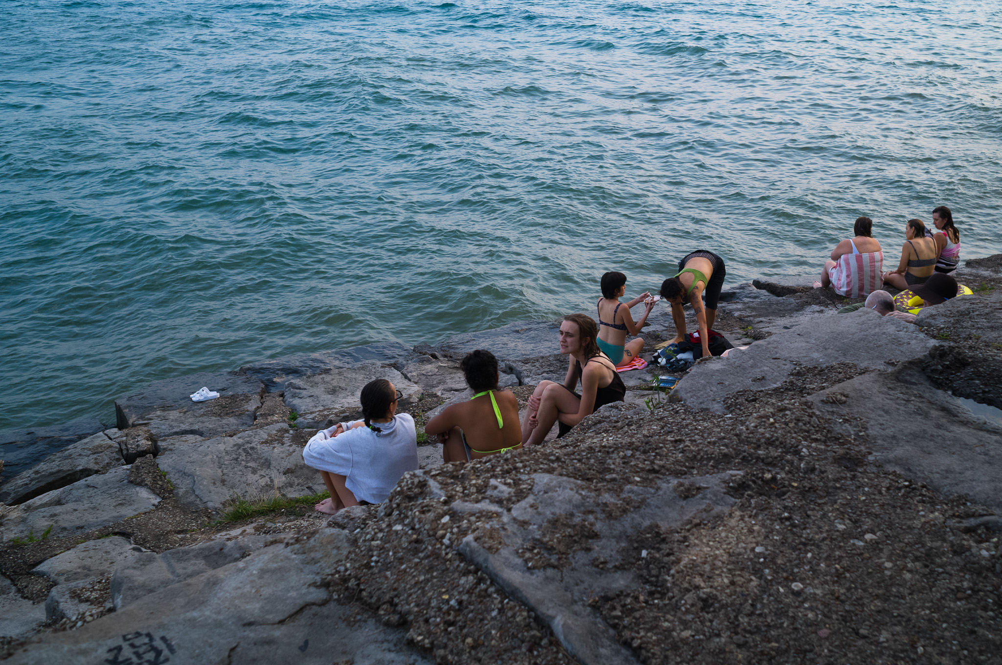 Christian Solorzano — photograph of a group sitting together on the lakefront rocks at dusk after swimming