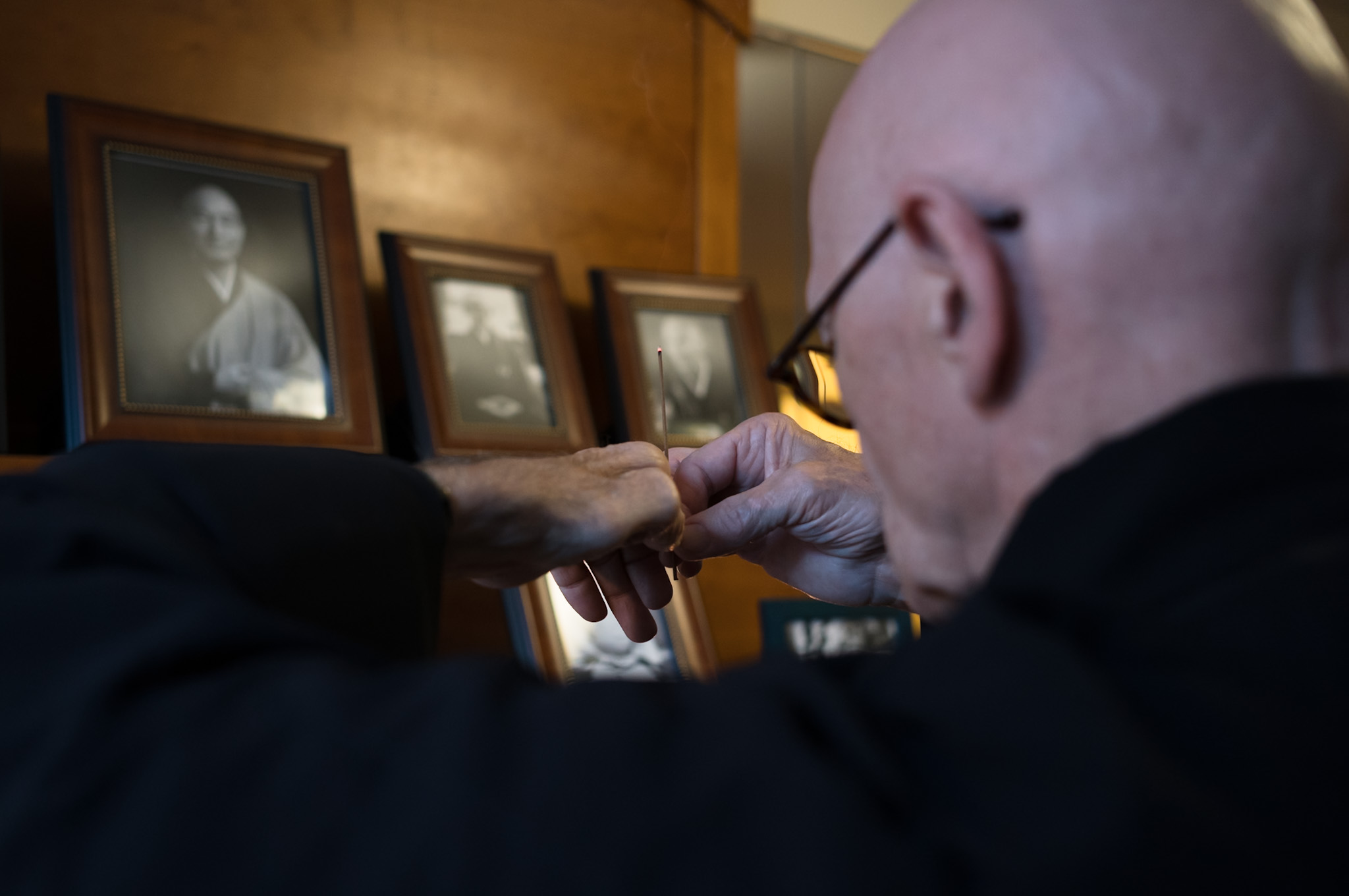 Hands holding a stick of incense in front of three framed portraits of teachers.
