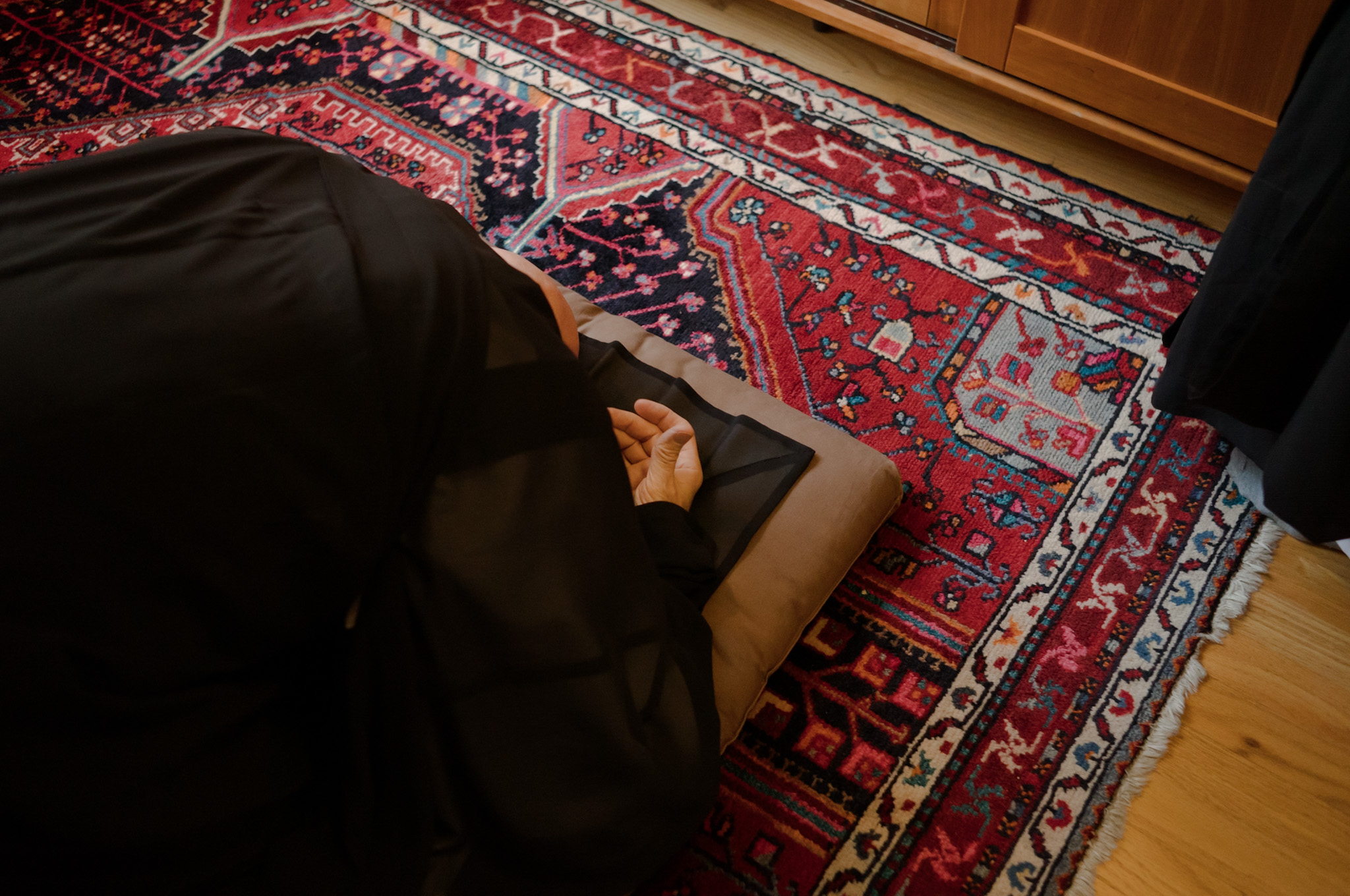 Looking down on a full bow, hands turned upward on a cushion at the edge of a red rug.