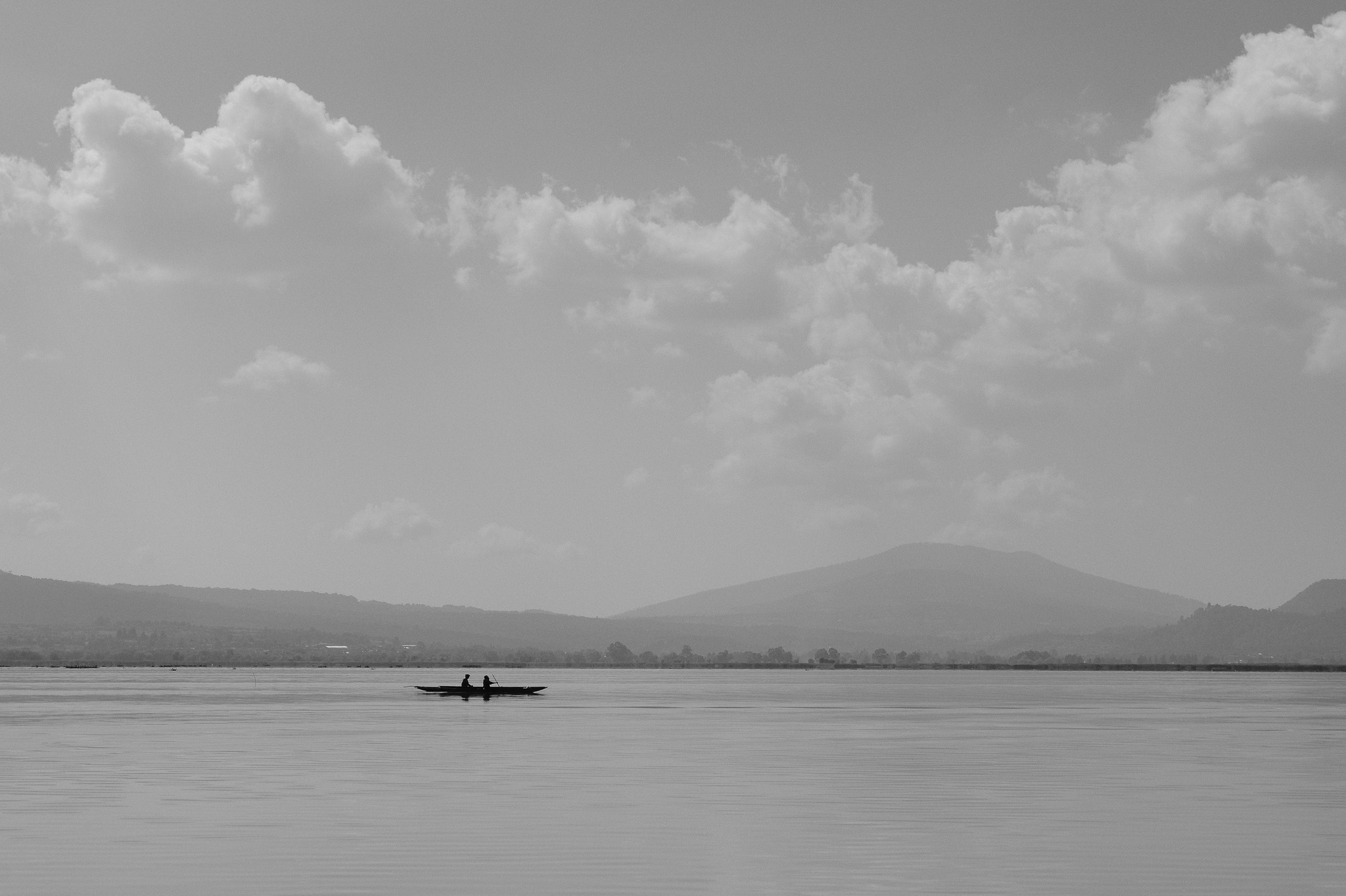 Christian Solorzano — minimalist black-and-white photograph of two people in a small boat on a vast calm lake below distant hills