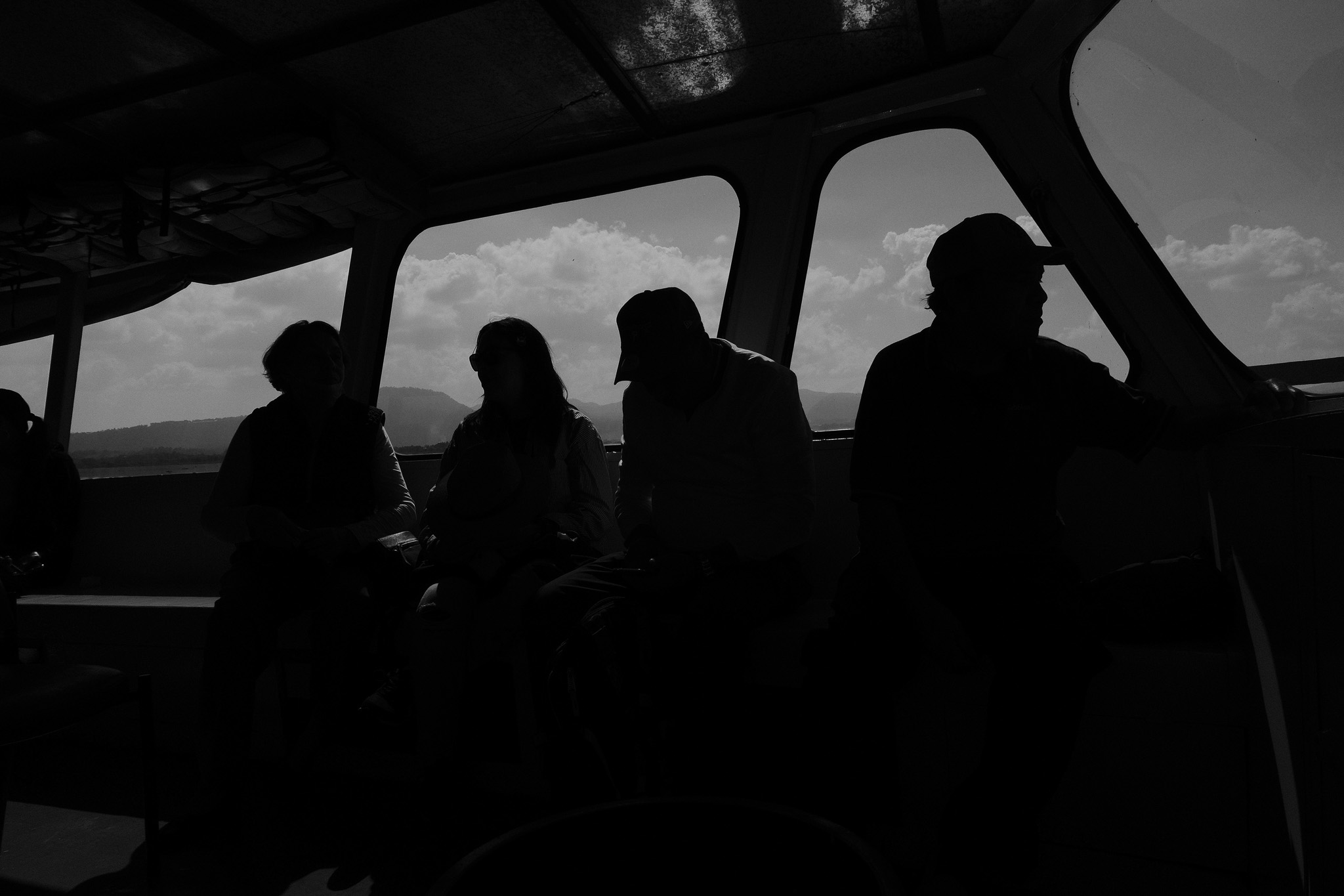 Christian Solorzano — black-and-white photograph of silhouetted passengers gazing out the windows of a boat