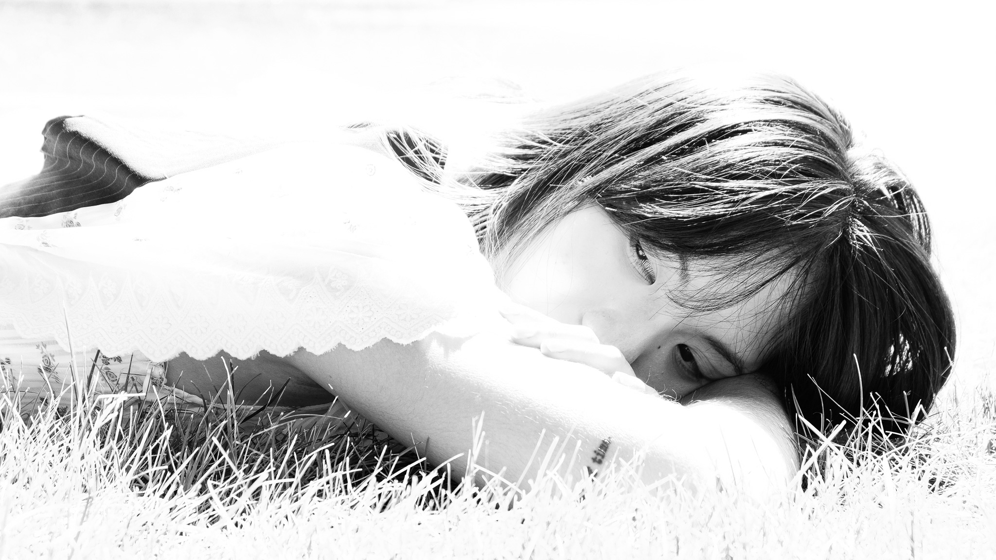 Christian Solorzano — high-key black-and-white portrait of a young woman resting in tall grass