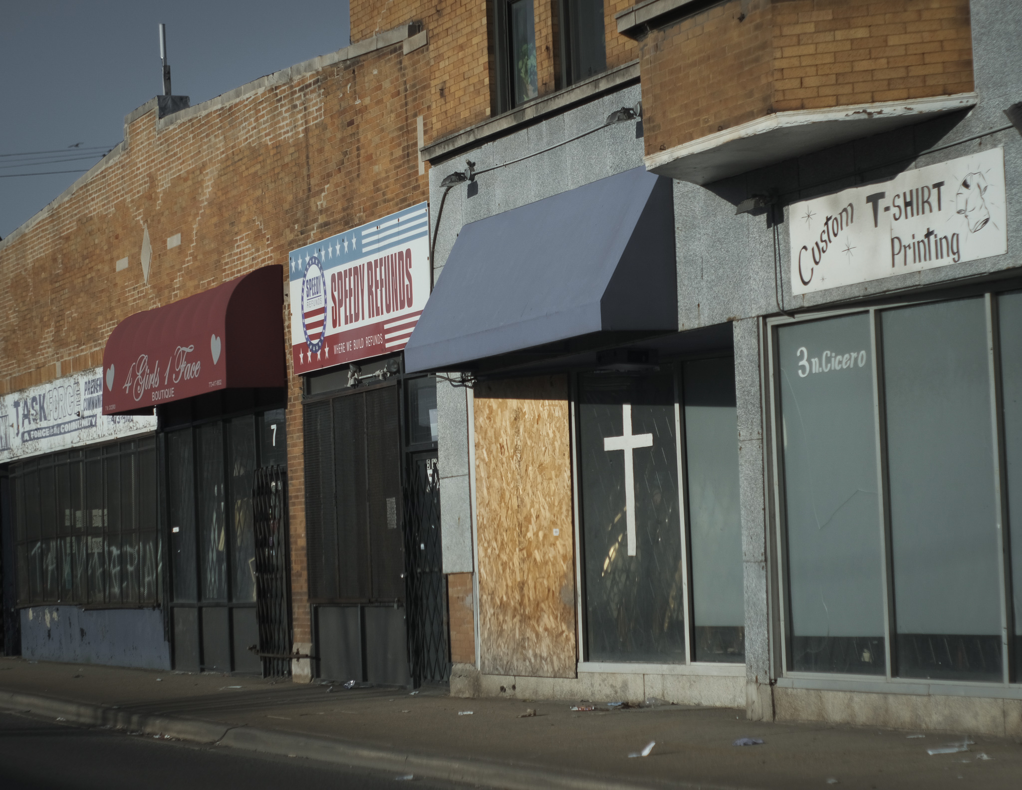 Christian Solorzano — photograph of a Chicago storefront row with a white cross painted on a boarded window