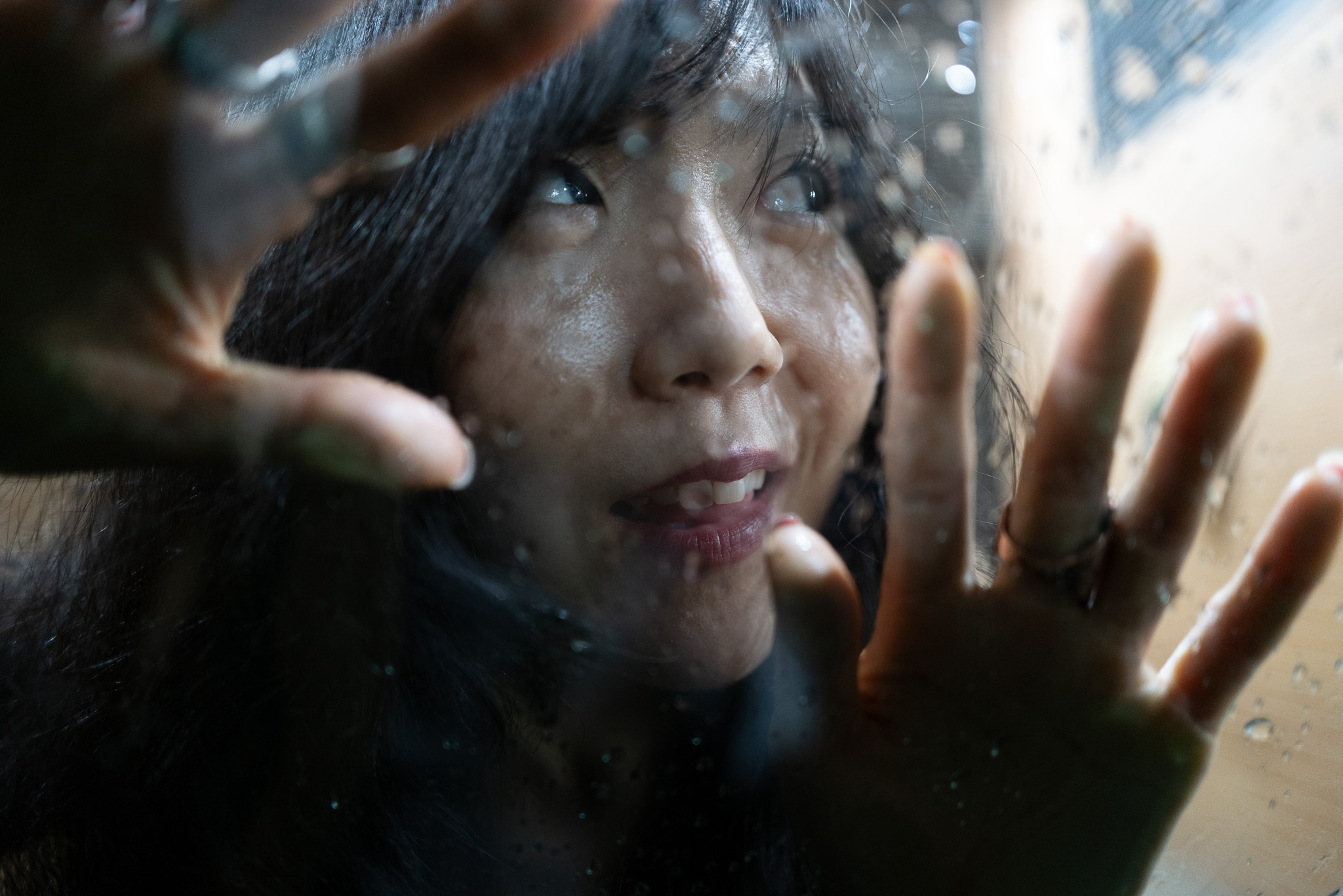 Christian Solorzano — photograph of a woman pressing her face and hands against a rain-streaked window